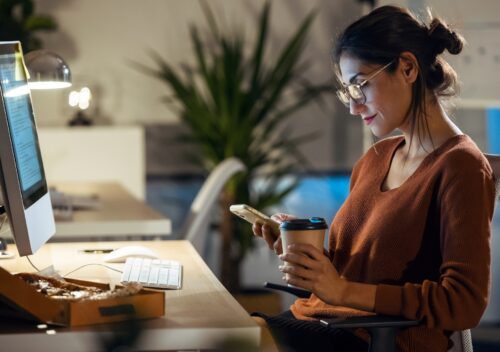 Beauty business woman sending messages with mobile phone while working with computer in the office.